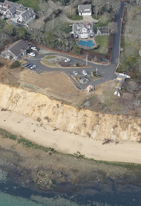 an aerial view of an eroding coastal bluff on a national wildlife refuge property. Buildings, a parking lot and trees can be seen surrounding the property