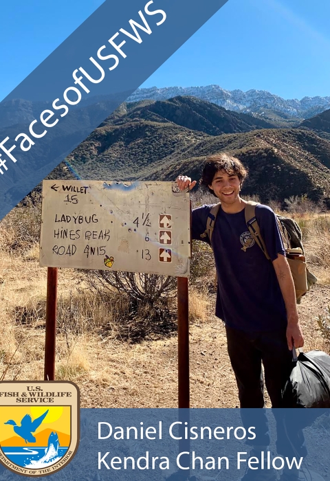 A man standing next to an outdoor sign. A banner reads "#FacesofUSFWS" and another banner reads "Daniel Cisneros Kendra Chan Fellow"
