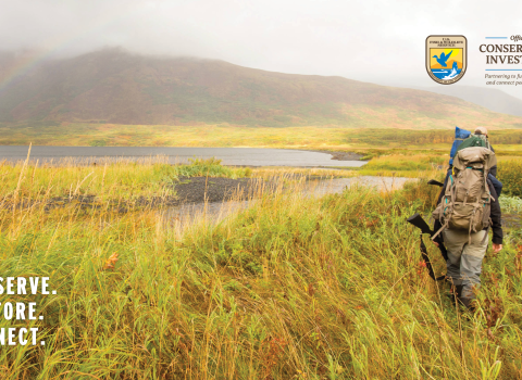 Two hunters with backpacks and firearms walk through Kodiak National Wildlife Refuge.