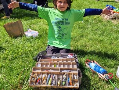 Kid kneeling in front of a tackle box with fishing lures inside