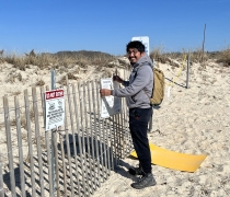A smiling man posts a sign on a snow fence.