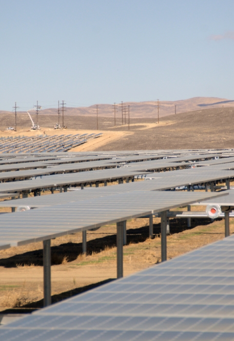 Rows of solar panels in arid grassland with foothills in the distance.