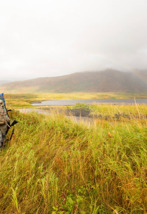Two hunters with backpacks and firearms walk through Kodiak National Wildlife Refuge
