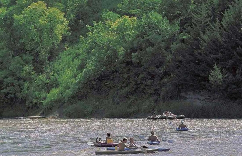 Kayakers and rafters on a river with a steep bank covered in green foliage
