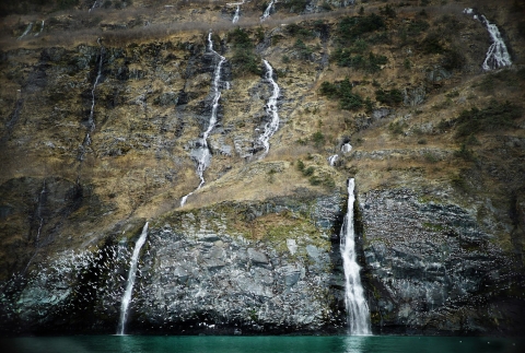 a cliff face with waterfalls and birds flying in front