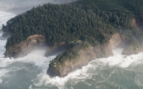 A huge rocky headland covered in trees and surrounded by the rolling Pacific Ocean