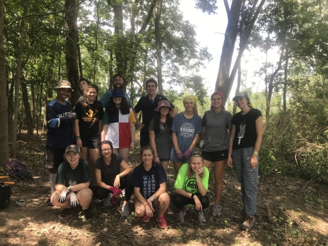 Group of 14 students pose in a forest setting