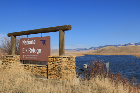 A sign reading "National Elk Refuge" positioned next to a wide creek.