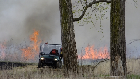 Prescribed burn of grassland unit with fire in background and UTV in foreground