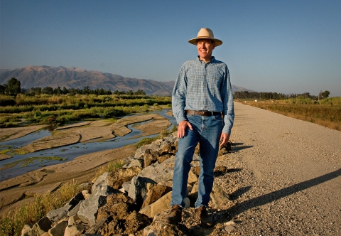 A man wearing a hat standing on the side of the road near a river