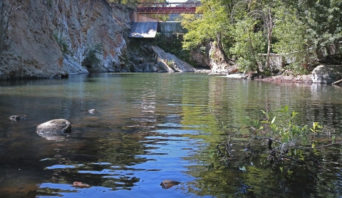 Landscape photo of a river with rocks and a dam the background.