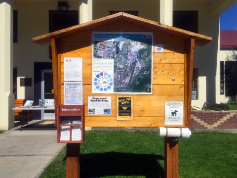 A signboard is in front of the hatchery, with a map displayed, miscellaneous signs, a box with information flyers, and a container for dog poop bags.