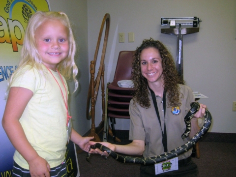 Stacy holding a king snake while a little girl touches its tail and smiles for the camera.