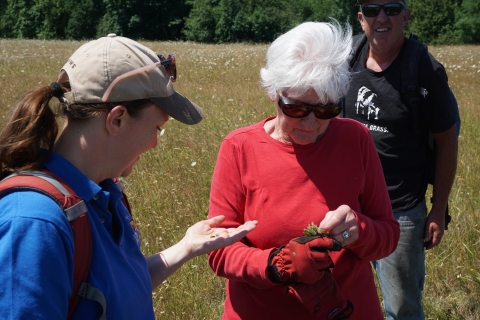 A woman in a red shirt and sunglasses shows seeds to a US Fish & Wildlife staff person in a baseball hat and blue shirt