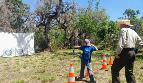 A child shooting an arrow at a target with a refuge employee looking on.