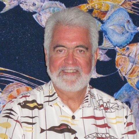 Rick Gaffney smiles at the camera. He is wearing a white shirt with fish patterns on it. 