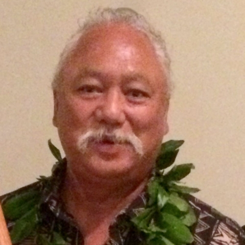 Sol Kaho’ohalahala smiles at the camera. He is wearing an aloha shirt and lei.