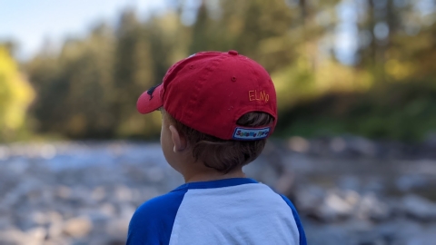 Child in red hat gazes at tree-lined river