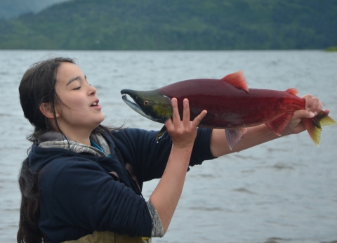 Aquatic Science Academy student holds a red salmon in front of her face. 