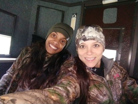 Picture of two female hunters wearing knit hats and camo gear in a hunt blind
