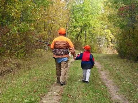 A man and son wearing orange hats walk together on a trail