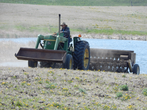 A man drives a tractor pulling a grass drill over a stretch of arid land