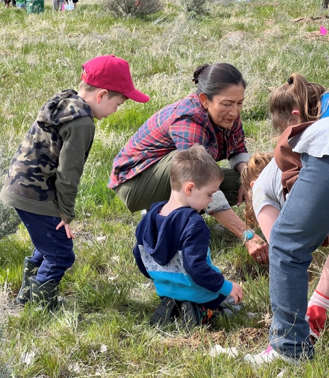 A woman and children plant small sagebrush plants together on a grassy hillside.