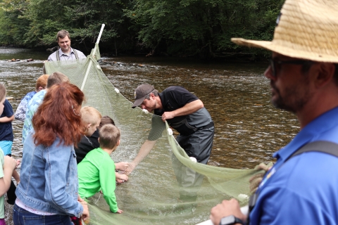 Three adults hold a kick seine as students pull fish from it.