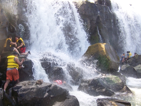 People in yellow life jackets are on and around rocks working to harvest lamprey in front of a rushing waterfall.