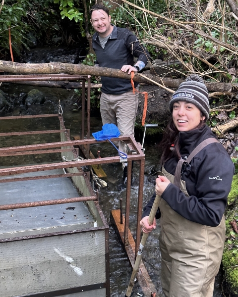 Bethany and Josh Fackrell standing in a creek beside a Kokanee Salmon fry trapping device.