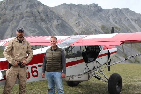 Federal Wildlife Officer Cody Smith poses with Congressman Ed Case in front of a Refuge LE Top Cub on a remote airstrip within Arctic National Wildlife Refuge