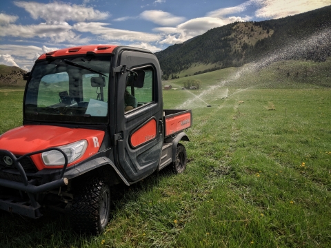 A red orange UTV in a green field with sprinklers and nearby mountain.