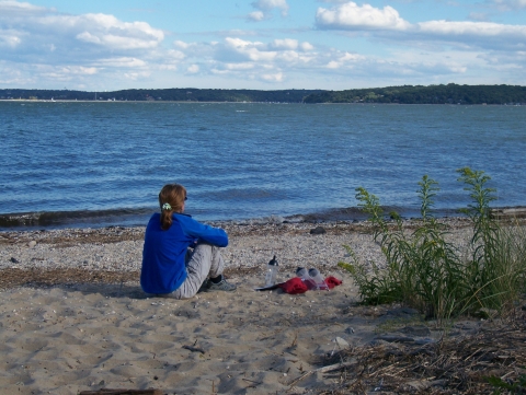 A woman sits on the beach and looks out onto the bay
