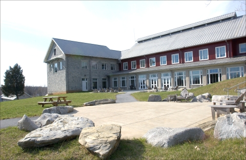 concrete patio with chairs and picnic table surrounded by large rocks and large building in background