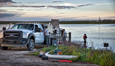 A truck, people and equipment by a river