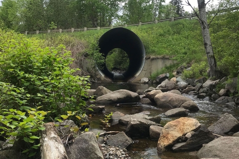 A large pipe crossing a stream, providing a pathway for water flow.