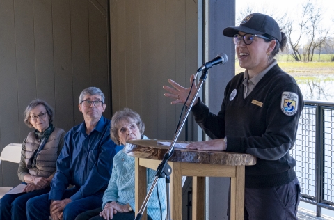 A person in a U.S. Fish and Wildlife Service uniform speaks at a microphone behind a podium.