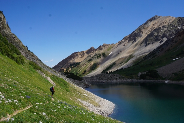 A backpacker in a bright valley overlooking a deep blue lake