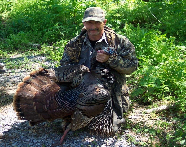Man wearing camouflaged clothes holding large tom turkey