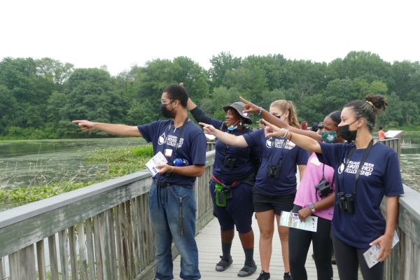 A group of young people with binoculars are pointing off the boardwalk. 