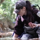 Female biologist kneeling in the water, one hand in the water, the other, cupped, holding mussels