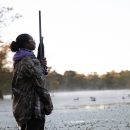 Young Woman In Hunting Gear Stands in wet-marsh at dusk.