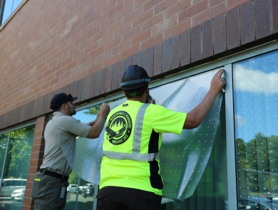2 men install bird-friendly materials on a glass window