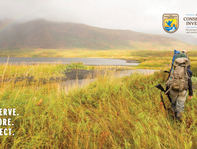 Two hunters with backpacks and firearms walk through Kodiak National Wildlife Refuge.
