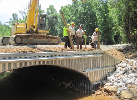 A construction crew stands atop a newly-installed culvert
