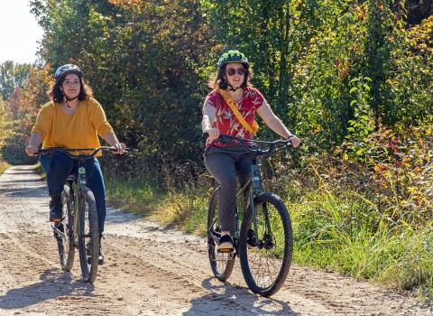 Two woman in bright clothing and helmets riding down a dirt road on electric assisted mountain bikes