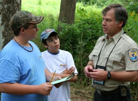 A man in a US Fish & Wildlife Service uniform talking to children in a forest