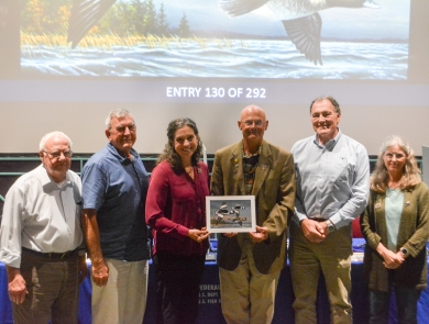 Six judges at the 2025 Federal Duck Stamp Art Contest hold the winning artwork.