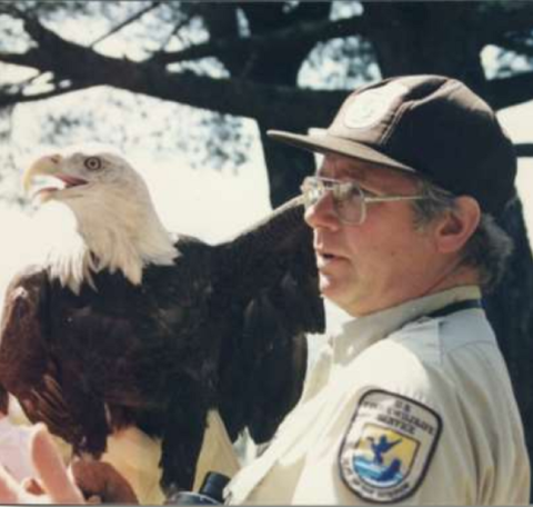 Man in Service shirt talks while a bald eagle perches on his arm