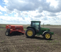 A John Deer Tractor and a Tye Grass-seeding Drill parked in a newly-seeded field.